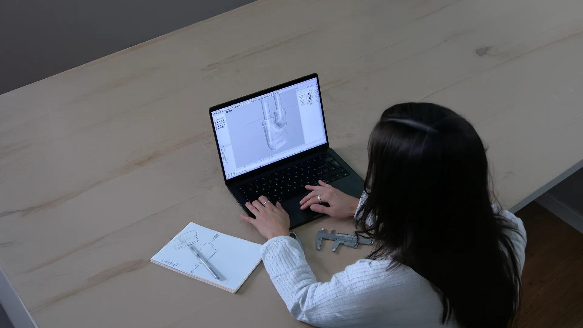 Person working on a laptop with a 3D CAD model